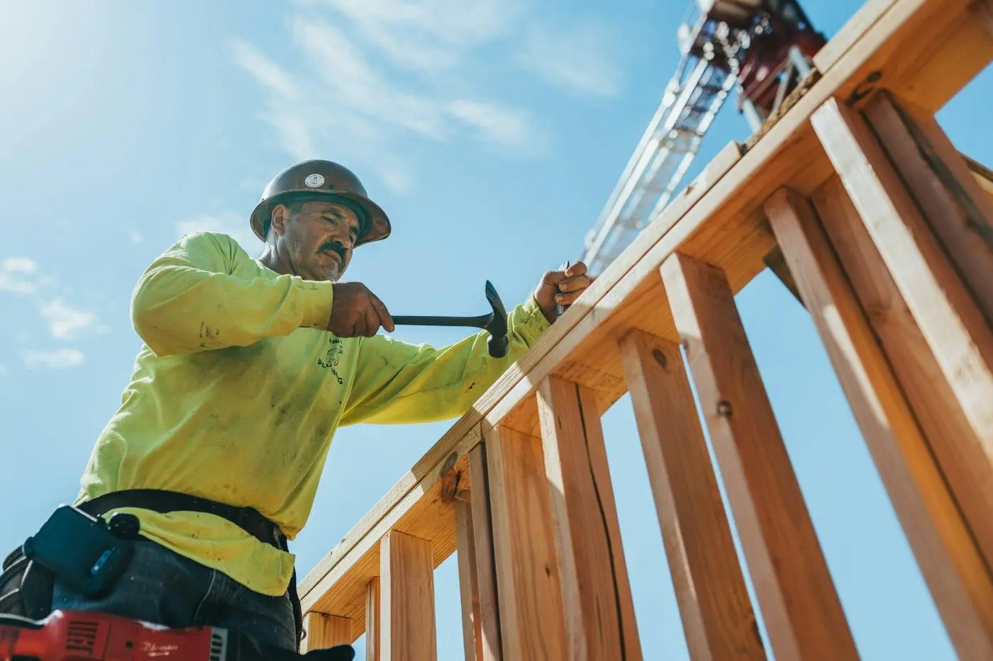 A carpenter framing a wall under a blue sky